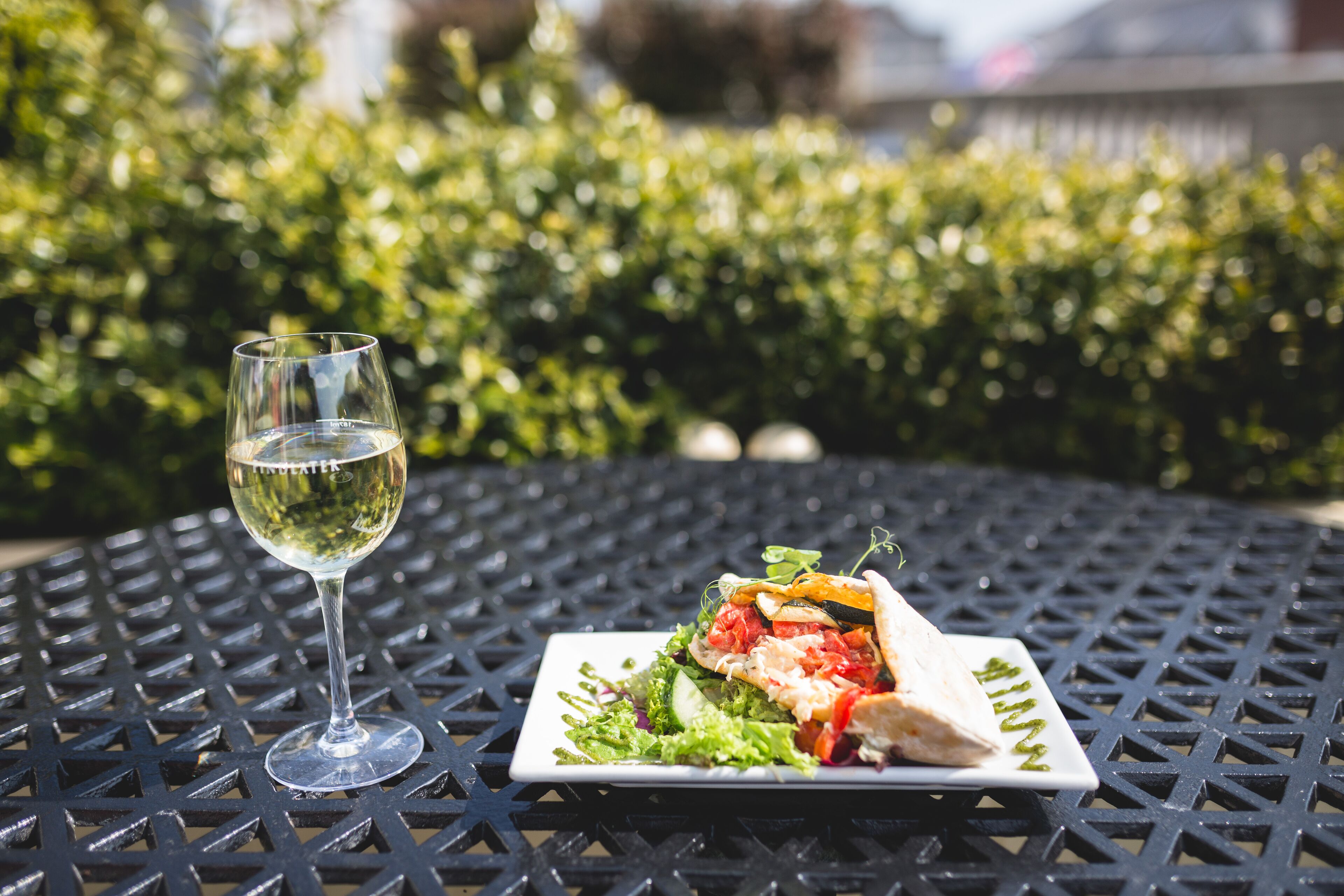 A square plate with a sandwich and a glass of white wine on a metal table.