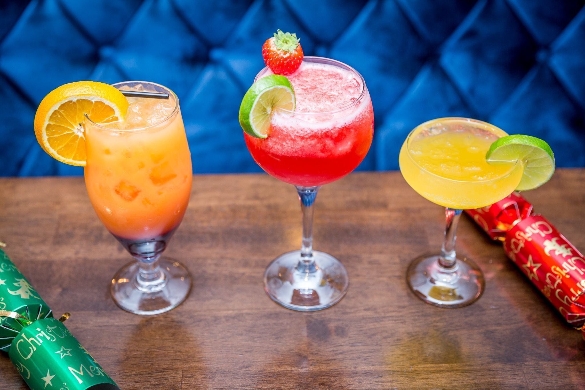 Three cocktails on a wooden table with Christmas decorations.