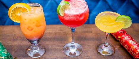 Three cocktails on a wooden table with Christmas decorations.