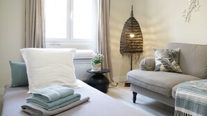 Un lit bien fait, avec des serviettes pliées, un canapé gris agrémenté de coussins à motifs et une lampe de sol décorative.
