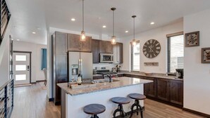 A modern kitchen with a central island, wooden cabinets, stainless steel appliances, and pendant lighting.