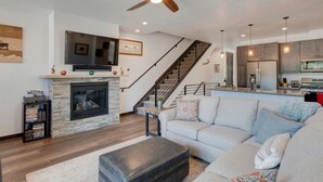 A modern living room with a fireplace, a sofa, a coffee table, and a staircase leading to the kitchen.