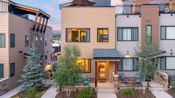 A modern multi-story residential building with a well-maintained front yard, outdoor seating, and a visible entrance.