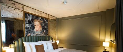 A hotel room with a large bed, a headboard with a mosaic design, a nightstand with a lamp, and a wall-mounted TV.