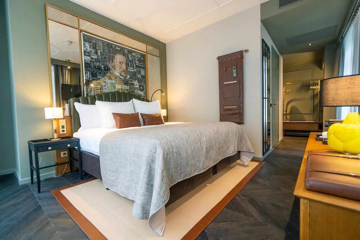 A hotel room with a bed, bedside table, lamp, and a large mirror.