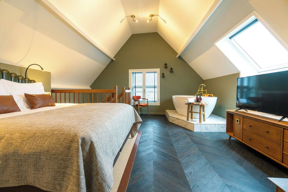Quarto com uma cama grande, uma cômoda de madeira, uma TV, uma janela e um claraboia.