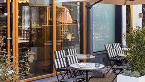 An outdoor seating area with tables and chairs, a glass storefront with signage, and a potted plant. - The Collector (The Hague)