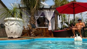 Ein Schwimmbecken mit klarem Wasser, umgeben von Palmen und einer Holzterrasse. Im Pool befindet sich eine weiße Schwan-Dekoration.
