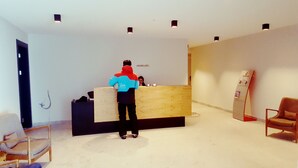 A reception area with a wooden reception desk, a chair, and a standing desk with a computer. - Beautiful and cozy studio style apartment (Gudauri)