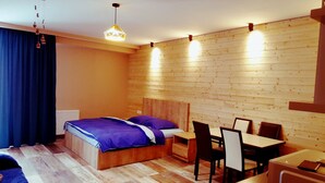 A modern hotel room with a wooden headboard bed, a desk, and chairs, and a large window with curtains. - Beautiful and cozy studio style apartment (Gudauri)