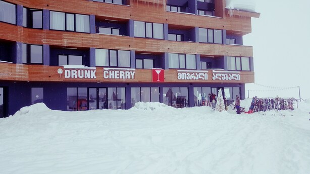 A multi-story building with a sign reading "DRUNK CHERRY" and another sign with non-English text. - Beautiful and cozy studio style apartment (Gudauri)