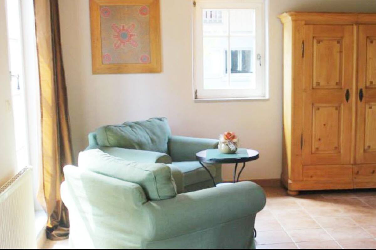 A room with a light green sofa, a small round table with a vase, and a wooden wardrobe.