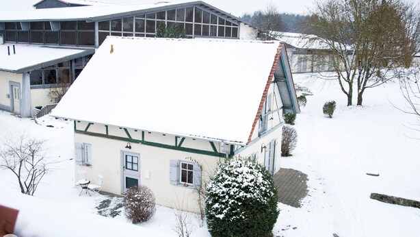 Ein zweistöckiges Gebäude mit geneigtem Dach, einer kleinen Veranda und verschneiter Landschaft.