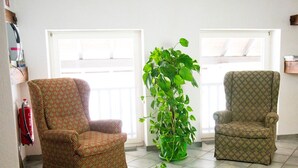 Ein Zimmer mit zwei gemusterten Sesseln, einer großen Grünpflanze und einem Feuerlöscher an der Wand.