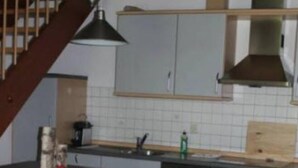 Eine Küche mit einer zentralen Kochinsel, einem Herd und einem Spülbecken. Zwei Hocker stehen an der Kochinsel.