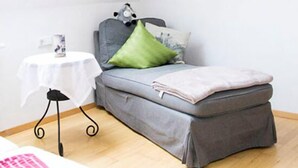 Ein kleiner, gemütlicher Raum mit schrägen Wänden, einem Einzelbett, einem Tisch und einem Fenster mit Tageslicht.