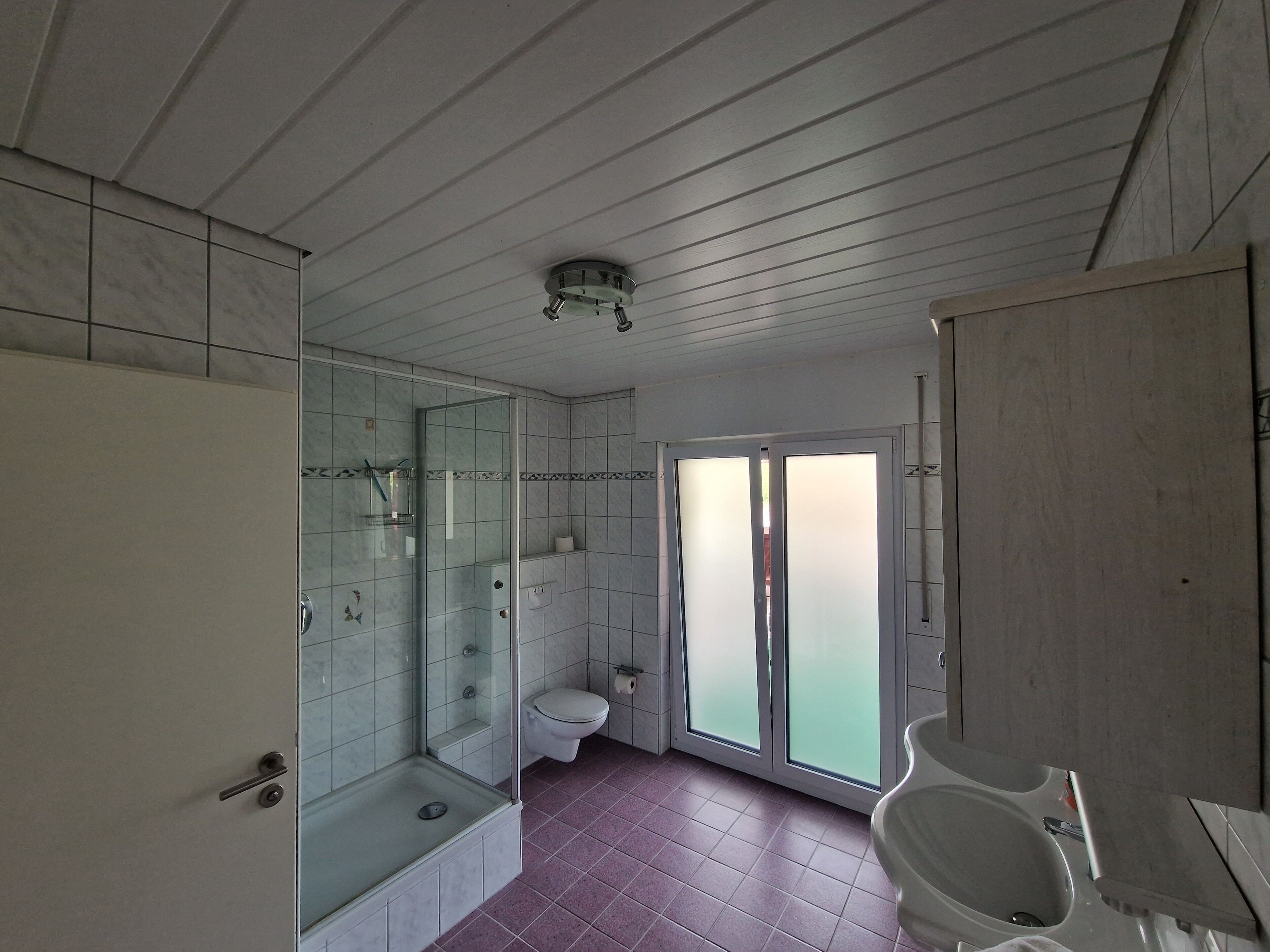 A bathroom with a glass-enclosed shower, a toilet, and a sink.