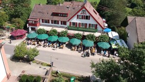 Un edificio de estilo europeo tradicional con tejado de tejas y un balcón. Hay zonas de estar al aire libre con sombrillas verdes.