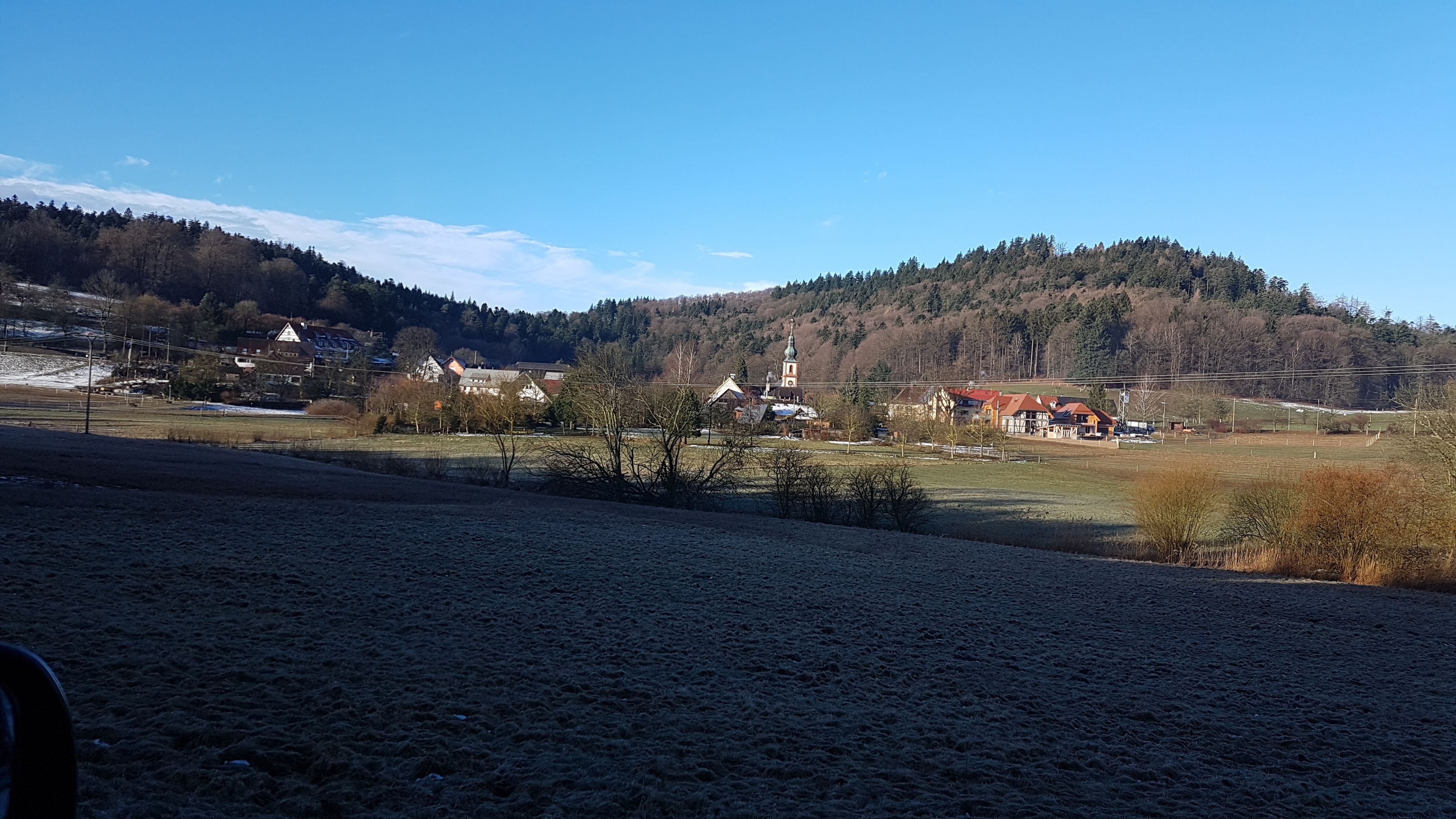 A rural landscape with a church, houses, and a hill in the background.