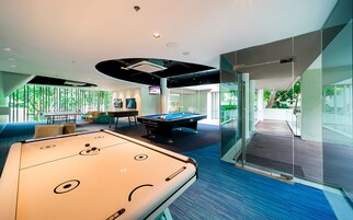 A modern indoor recreational area with a pool table, foosball table, and seating area with a view of greenery outside.