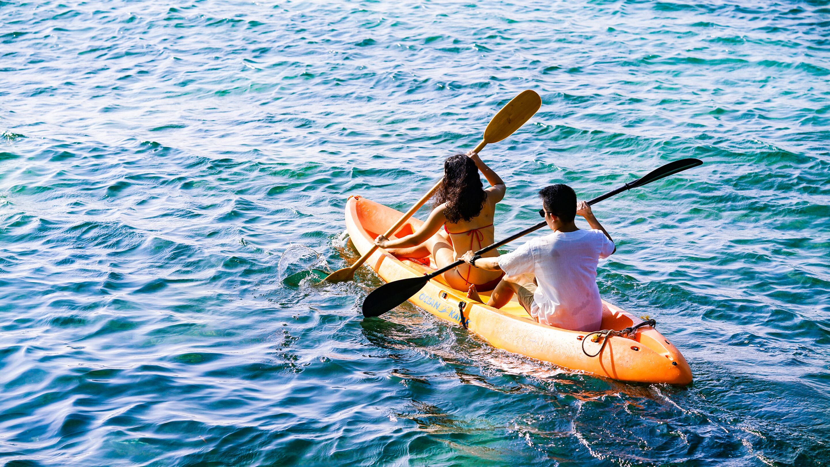 Deux personnes dans un kayak orange, sur une eau calme.