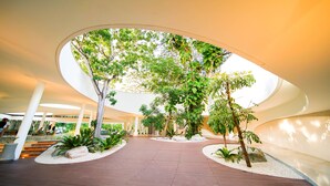An indoor atrium with a curved ceiling, surrounded by trees and plants, and a central open space with a wooden floor. - Tambuli Seaside Resort and Spa (Lapu-Lapu)