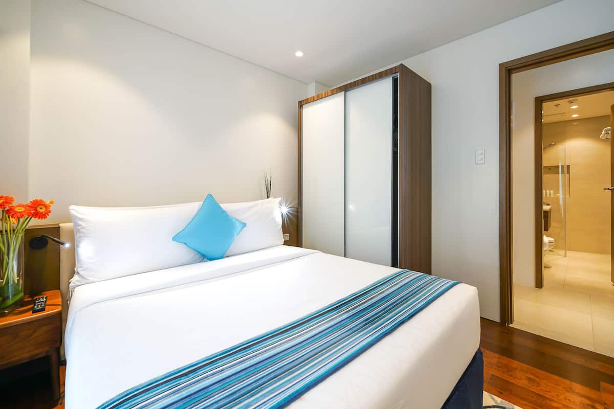 A hotel room with a bed, a nightstand, a vase with flowers, and a mirror.