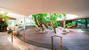 A spacious indoor atrium with a central tree, surrounded by seating areas and a glass railing. - Tambuli Seaside Resort and Spa (Lapu-Lapu)