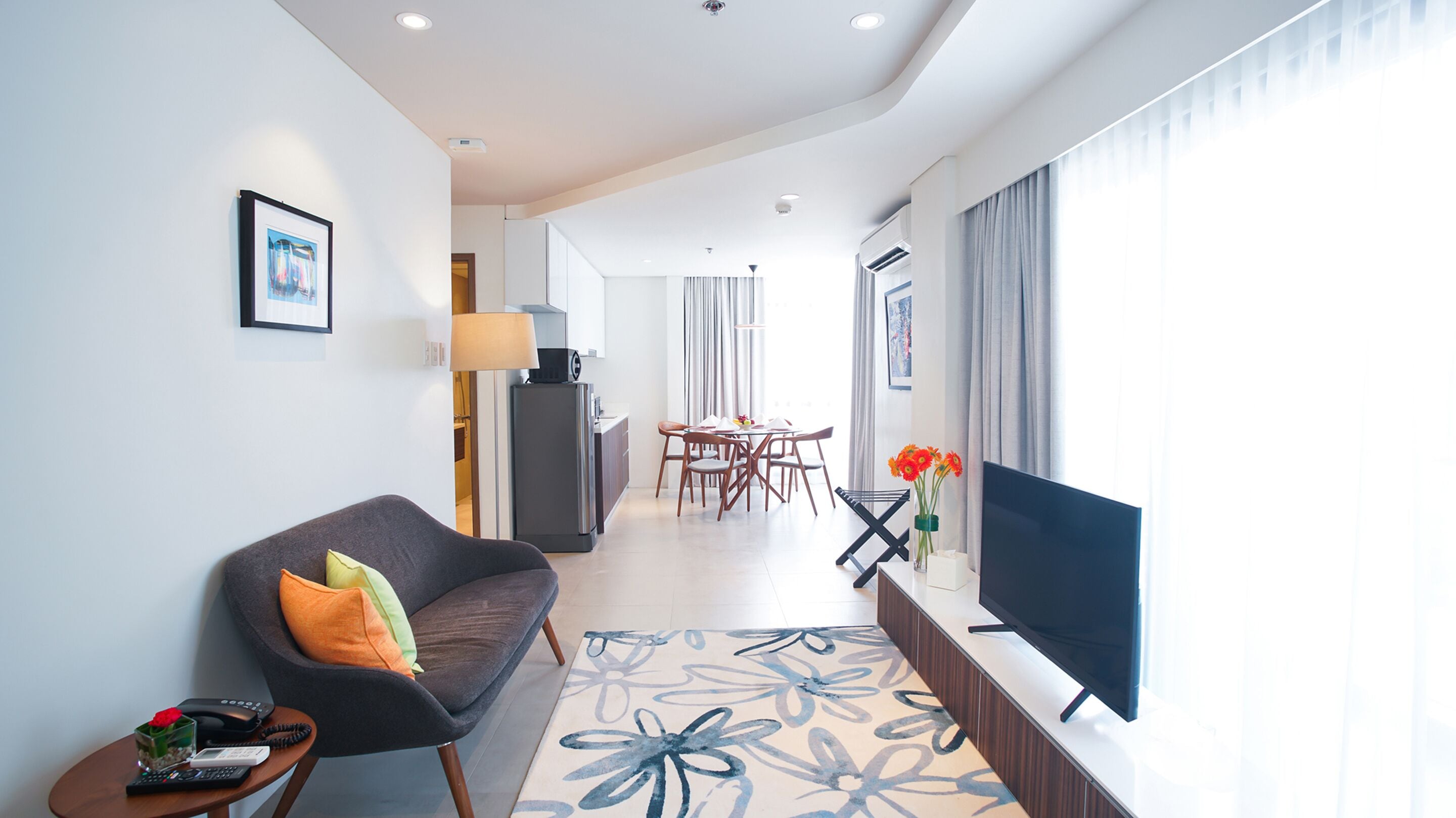 A modern living room with a sofa, TV, and a dining area in the background.