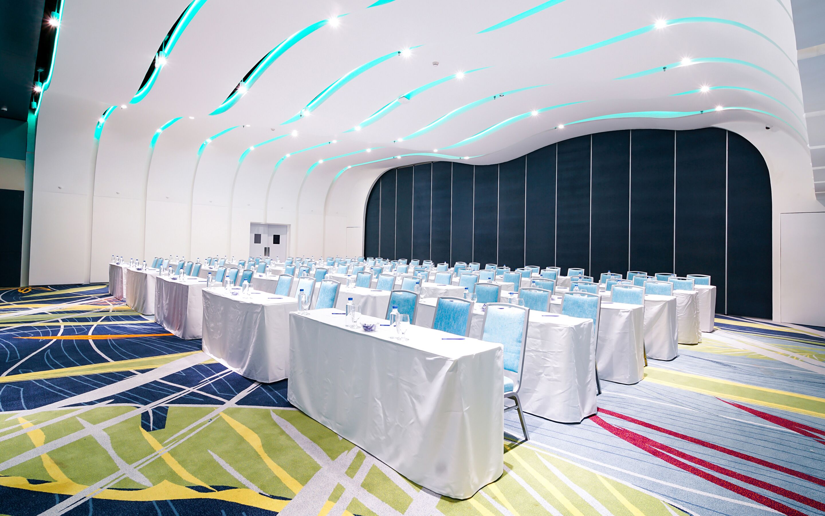A conference room with rows of tables, chairs, and a stage area.