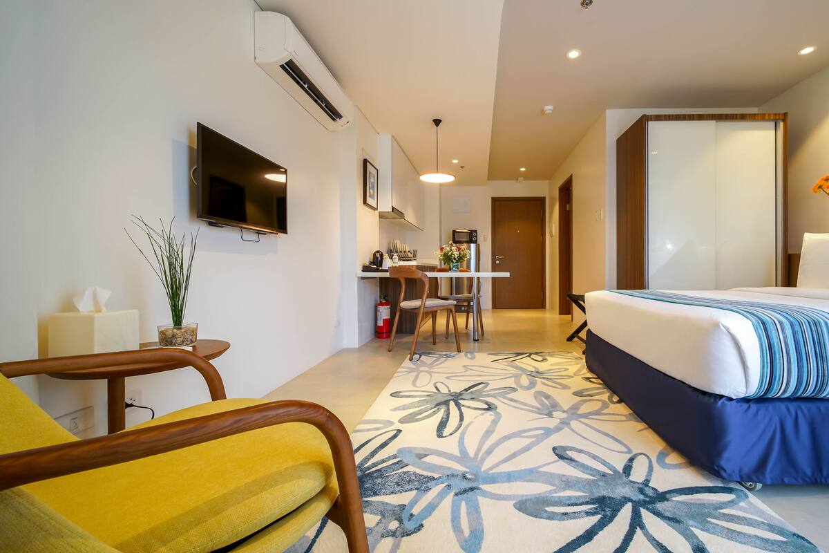 A hotel room with a bed, a desk, a chair, a TV, and a bathroom visible through an open door.