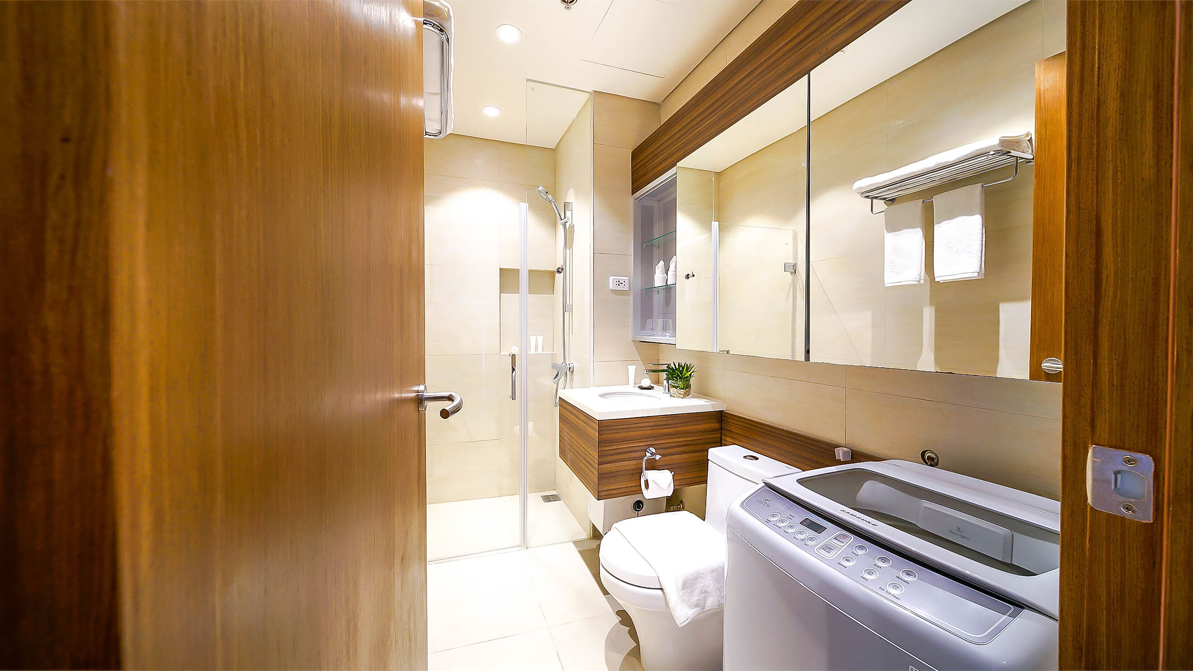 Une salle de bain moderne avec une porte en bois, une douche en verre, un lavabo, des toilettes et un lave-linge.