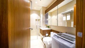 Une salle de bain moderne avec une porte en bois, une douche en verre, un lavabo, des toilettes et un lave-linge.