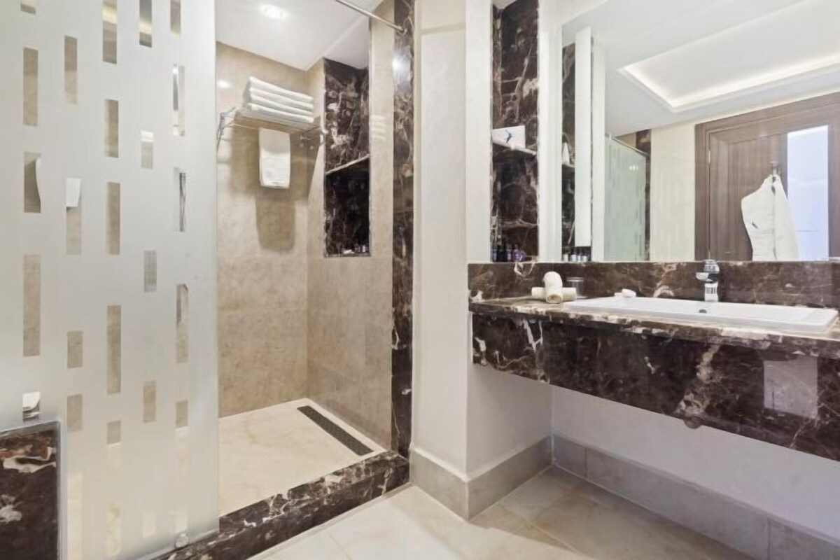 A modern bathroom with a marble vanity, a large mirror, and a glass shower enclosure.