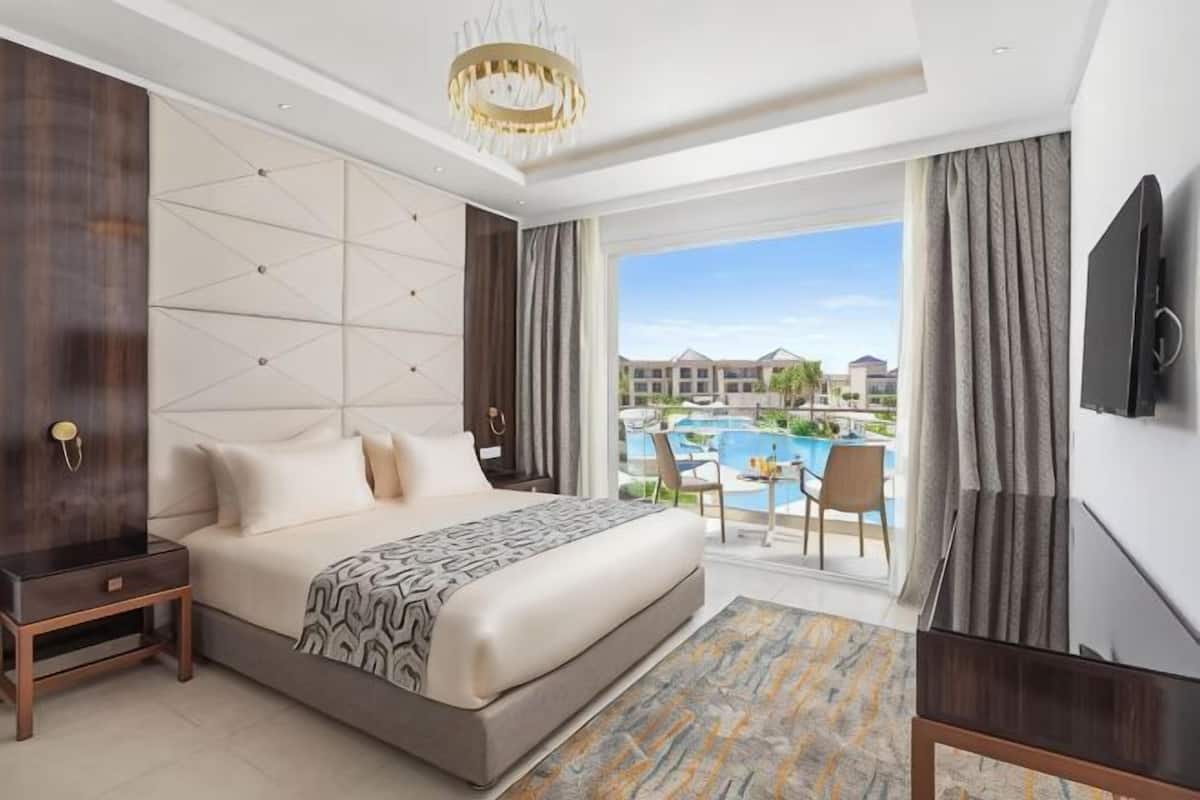 A hotel room with a large bed, a TV, a view of a pool, and a balcony.