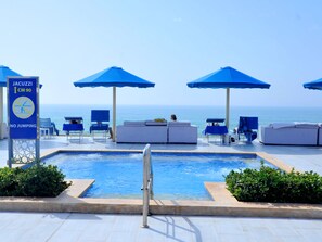 A poolside area with lounge chairs and umbrellas, a sign indicating a 90 cm depth, and a view of the sea. - Pickalbatros White Beach Taghazout - Adults Friendly 16 Years Plus - Ultra All Inclusive (Taghazout)