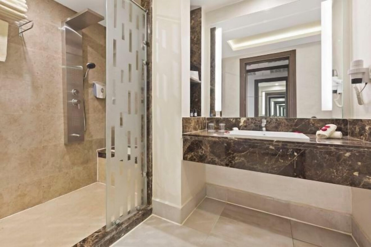 A modern bathroom with a glass-enclosed shower, a marble countertop, and a large mirror.