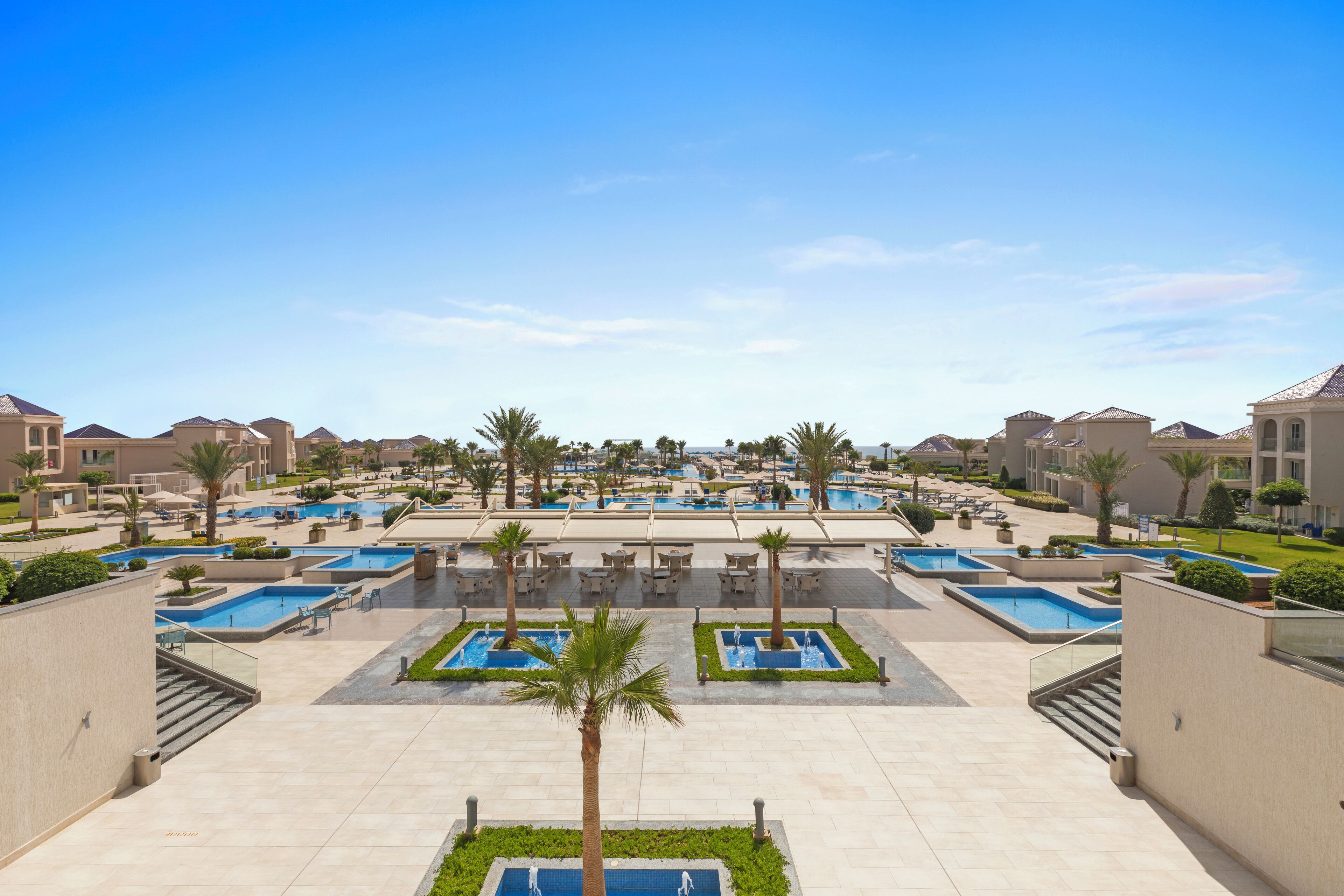 Un resort con varias piscinas, palmeras y un cielo azul despejado.
