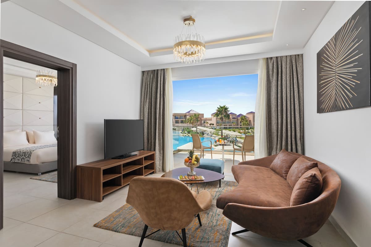 A modern living room with a sofa, armchair, TV, and a view of a pool and buildings.