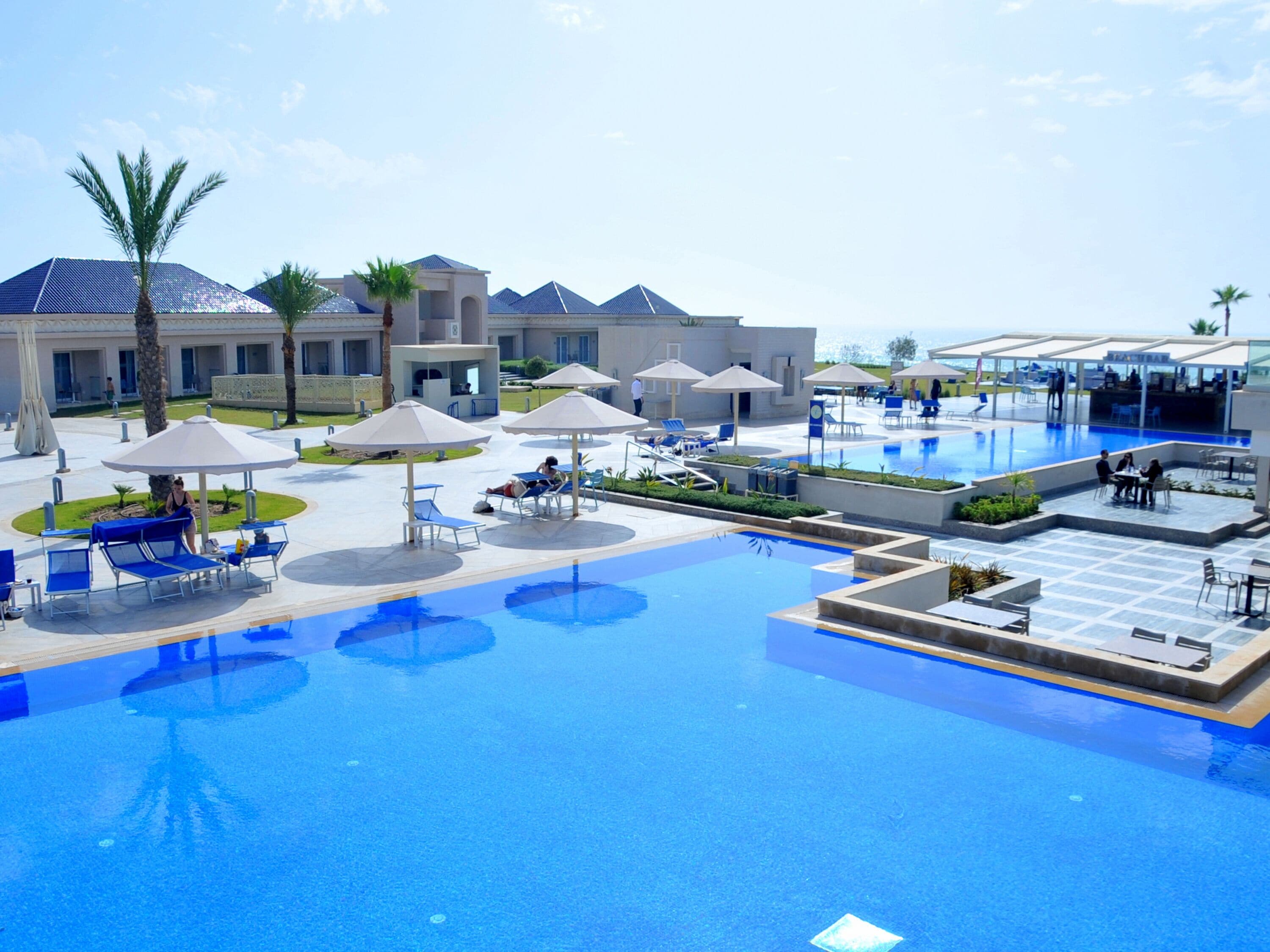 Un resort con una amplia piscina, camas de sol, sombrillas y un edificio de diseño moderno.