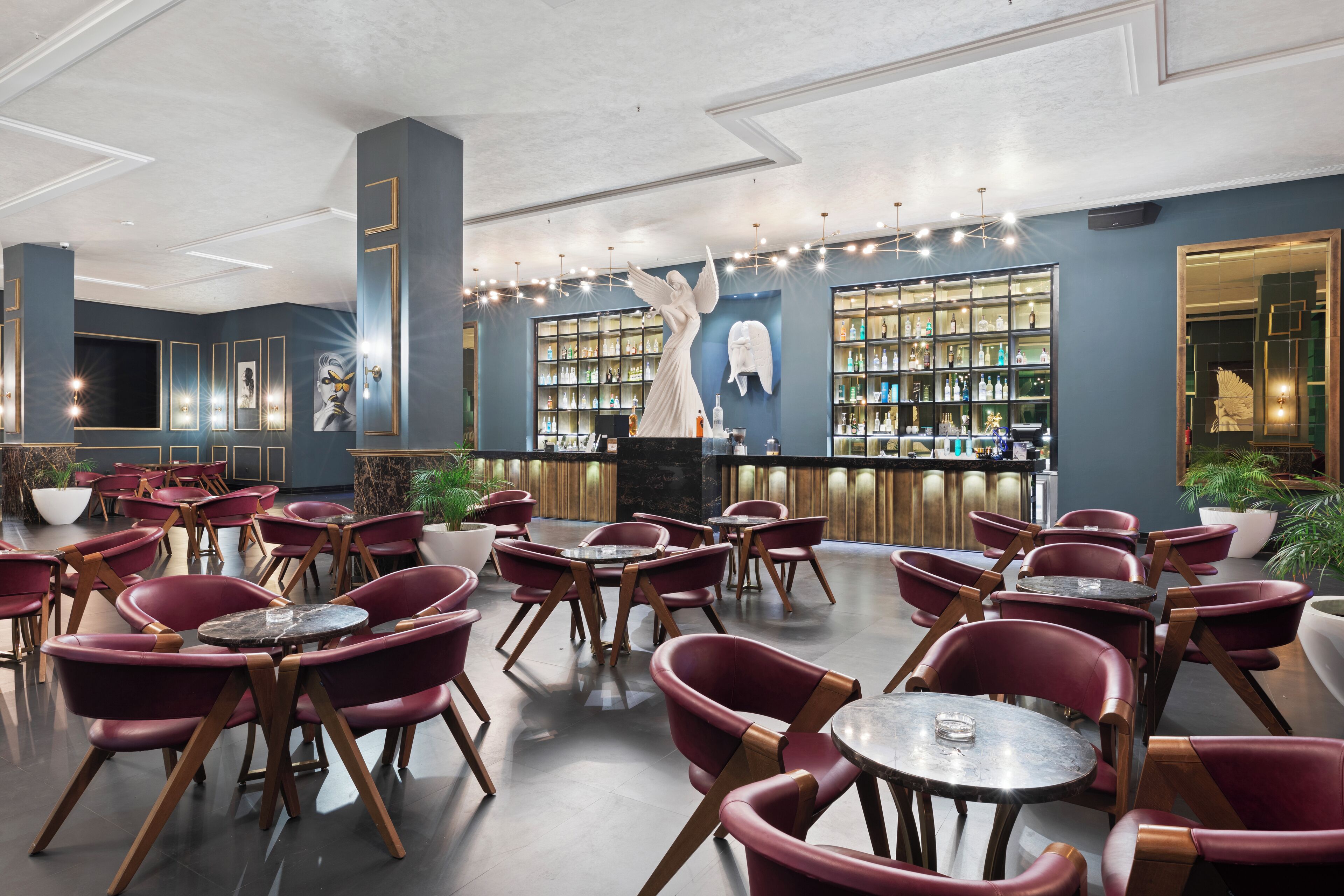 A modern bar area with a statue, red chairs, and a variety of bottles.