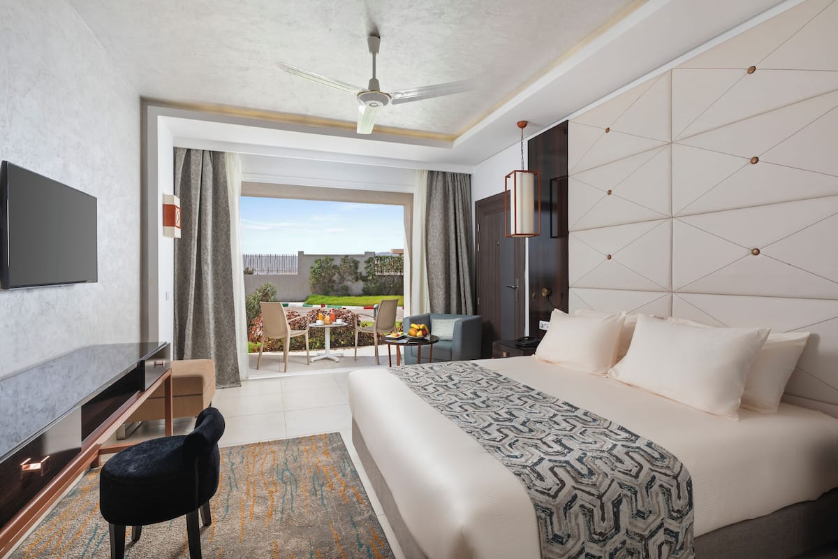 A modern hotel room with a large bed, a flat-screen TV, a desk, and a balcony with a view.