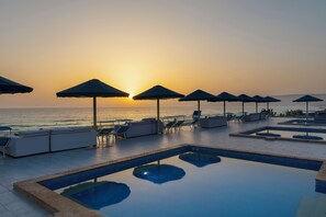 A poolside area with lounge chairs and umbrellas, overlooking the ocean at sunset.