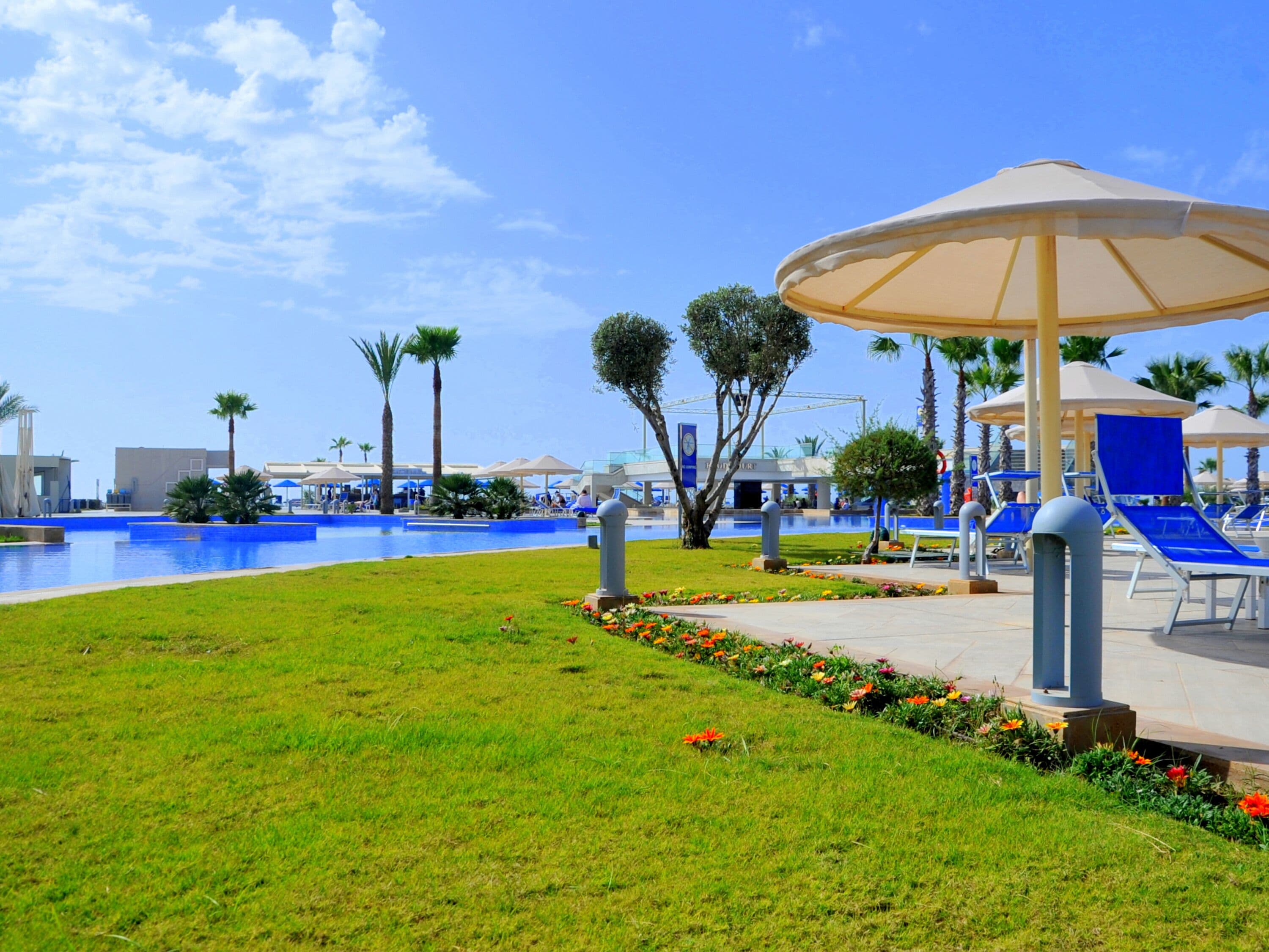 A pool area with lounge chairs and umbrellas, surrounded by well-maintained grass and flower beds.