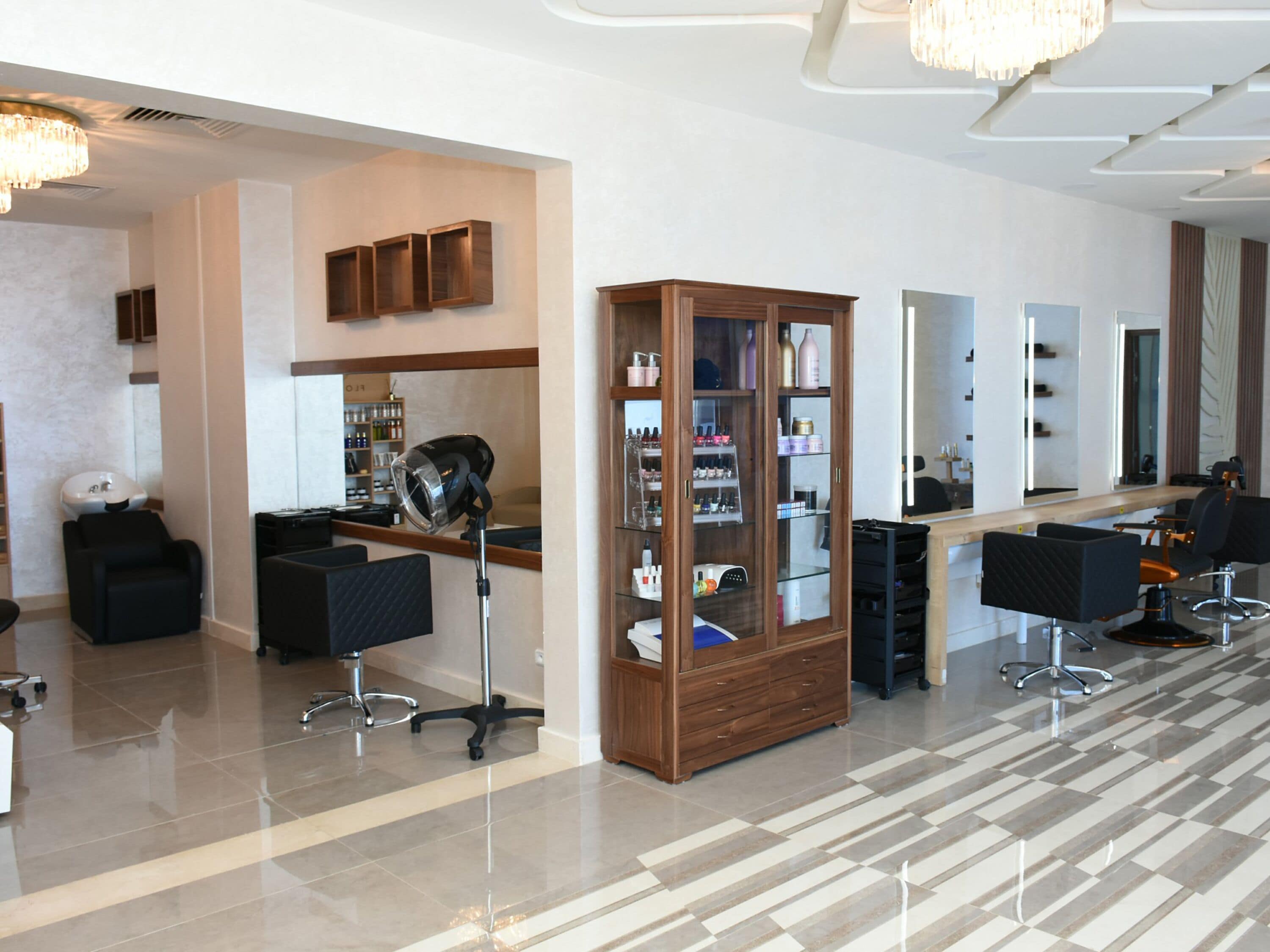 A modern salon with multiple hairdressing stations, a large mirror, and a cabinet filled with hair products.