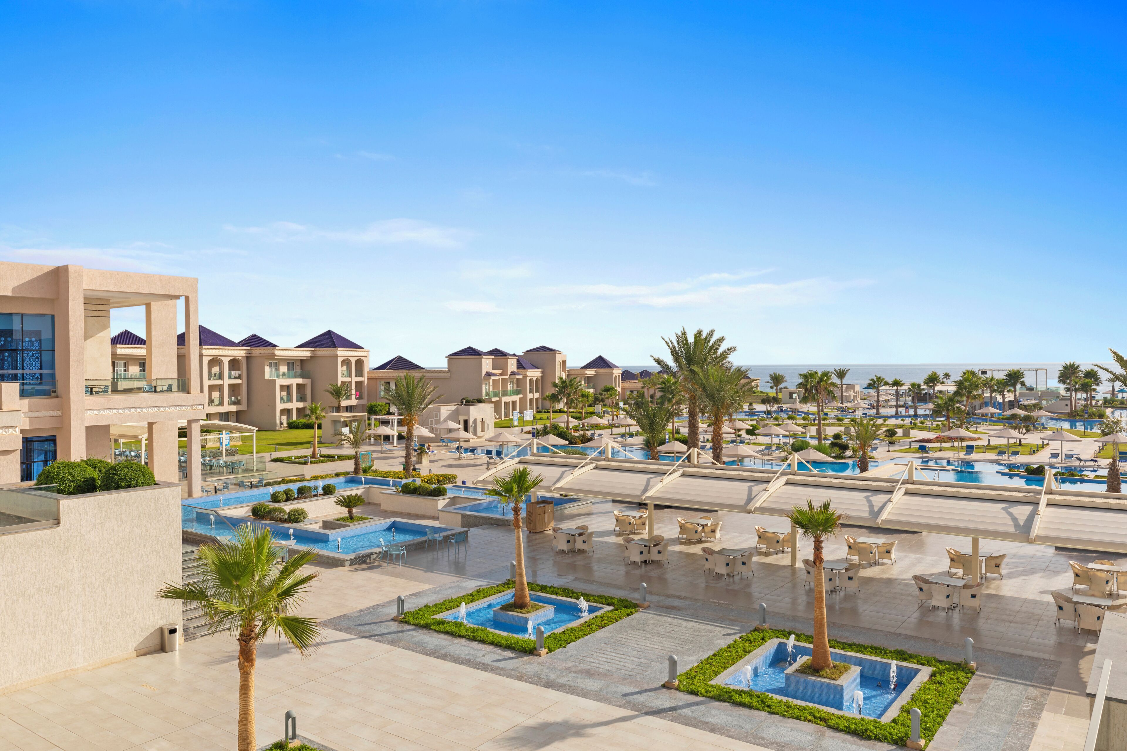 Un resort con varias piscinas, palmeras y zonas de estar al aire libre.