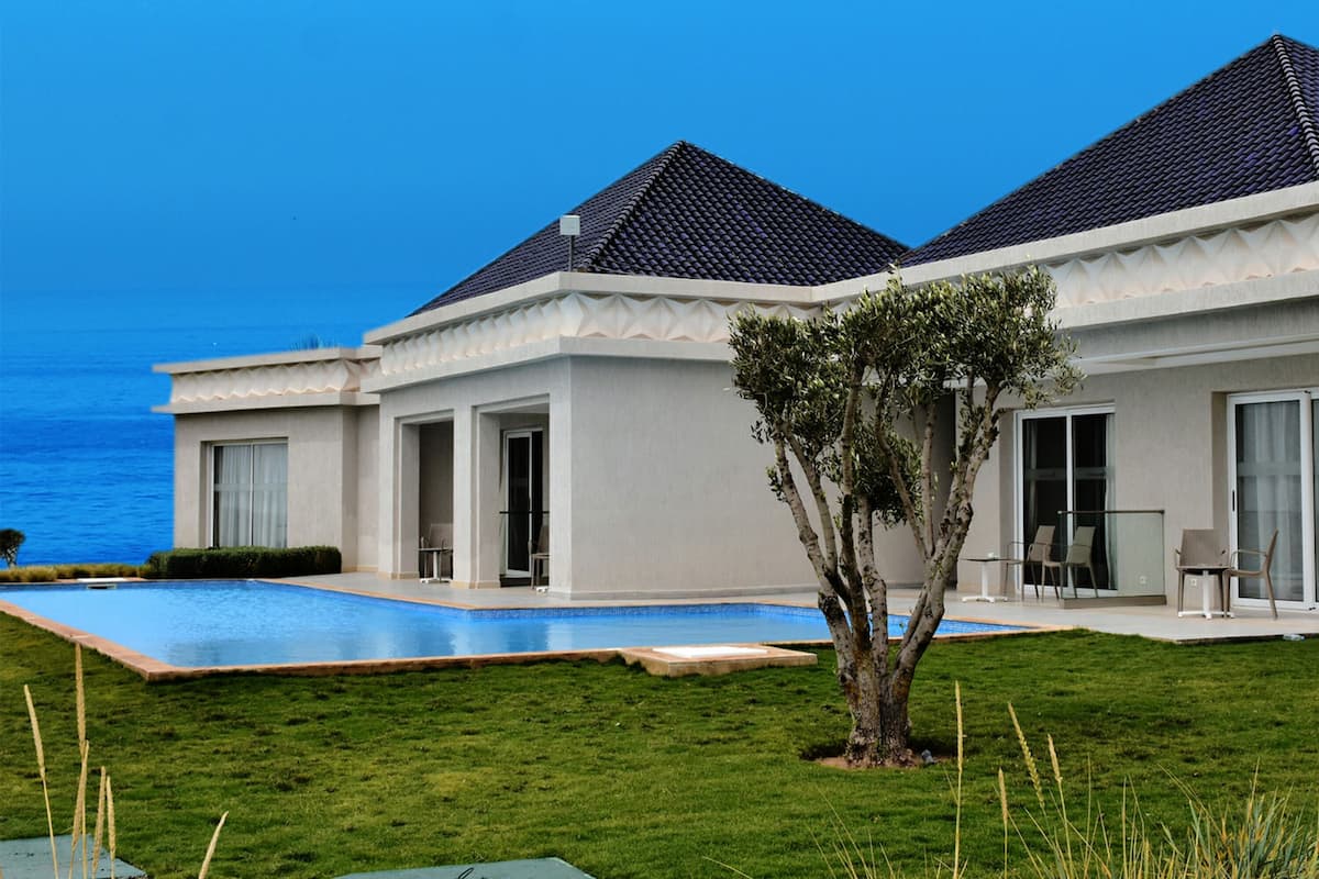 A modern house with a swimming pool, a tree in the front yard, and a view of the ocean.