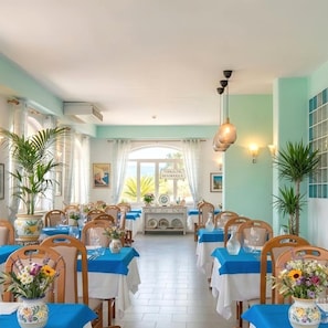A dining area with tables set for service, a view of the outdoors, and a decorative wall with a clock. - Hotel Park Victoria (Forio)