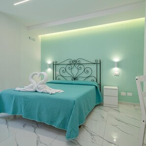A bedroom with a teal bedspread, a decorative swan towel, a black metal headboard, and two wall-mounted lights. - Hotel Park Victoria (Forio)