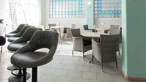 A restaurant with a row of bar stools, round tables, and wicker chairs. - Hotel Park Victoria (Forio)